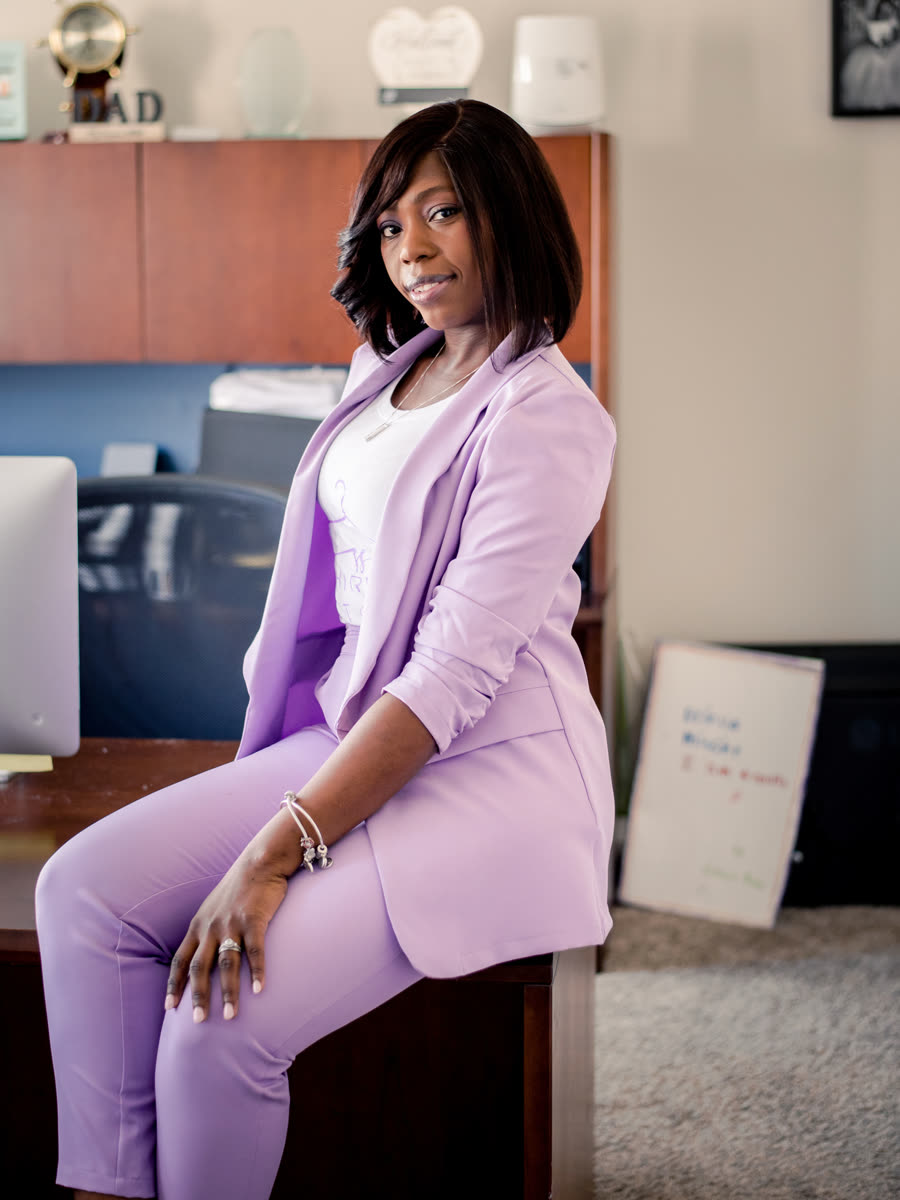 Bry sitting on the edge of her desk in her home office, in a lilac suit.