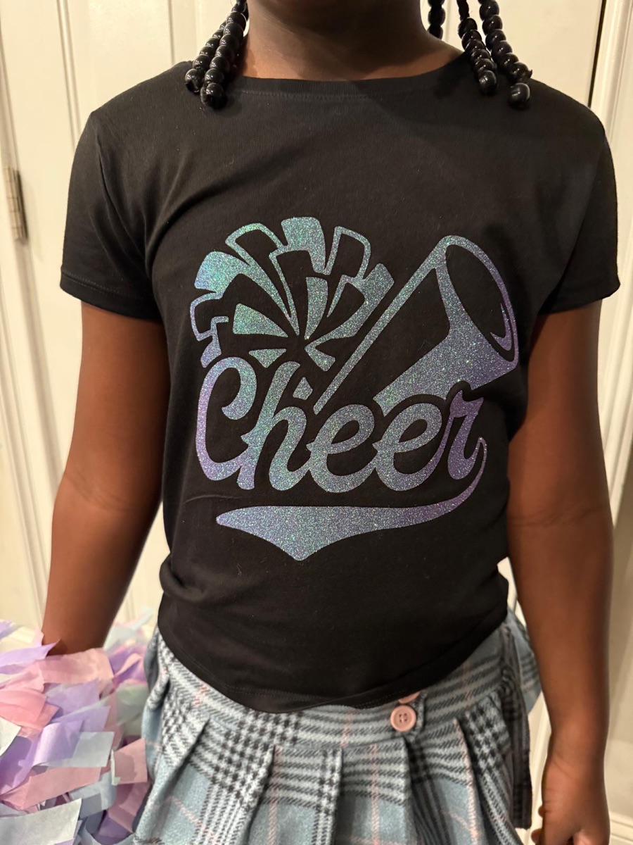 A black tee printed cheer in silver holographic glitter with pom-poms and a megaphone, worn with a plaid skirt.