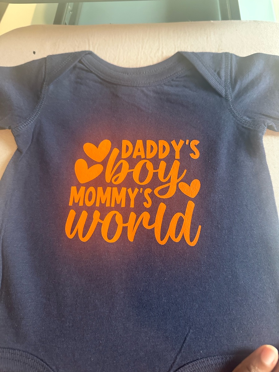A navy baby bodysuit printed daddy's boy, mommy's world in bright orange with small hearts.