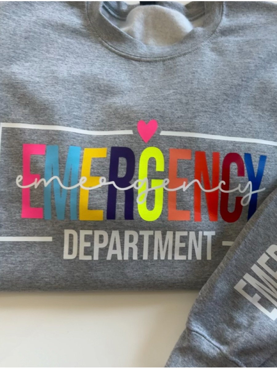 A heather grey sweatshirt printed EMERGENCY in rainbow letters over DEPARTMENT inside a white frame, with the words carried down the sleeve.