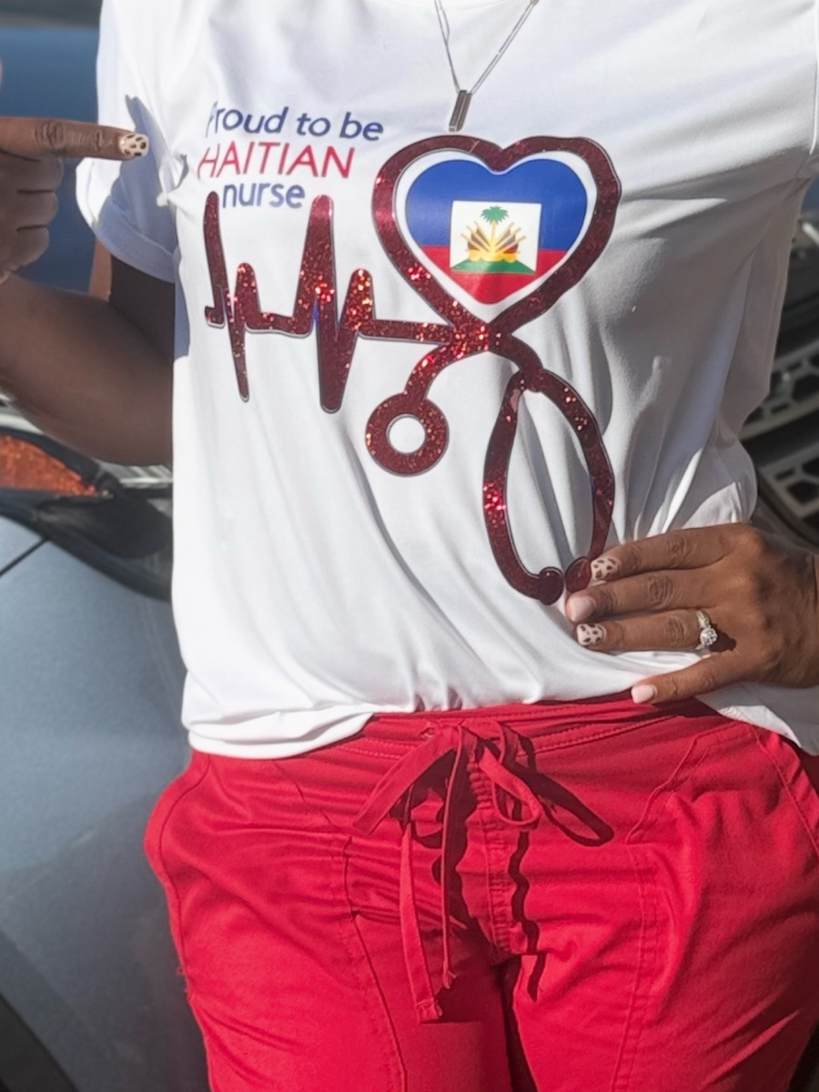 The Haitian nurse tee worn with red scrub pants, a thumb pointing at the print.