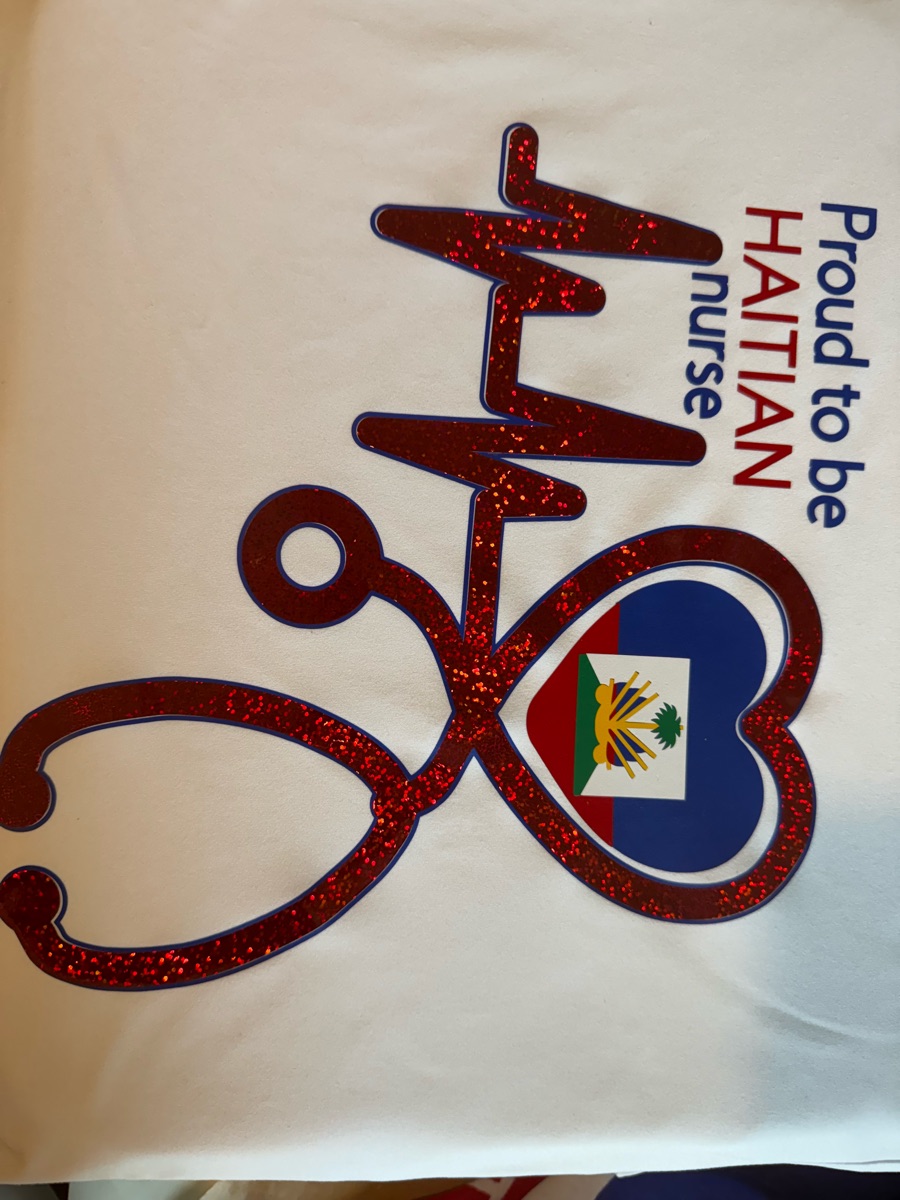 A white tee printed proud to be Haitian nurse beside a red glitter heartbeat line that turns into a stethoscope around a heart holding the Haitian flag.