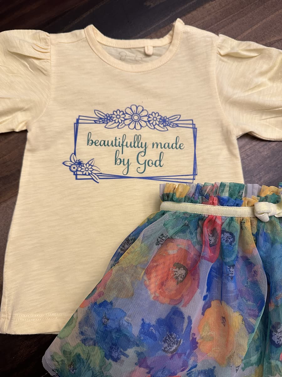 A cream toddler tee printed with beautifully made by God, paired with a floral tulle skirt.