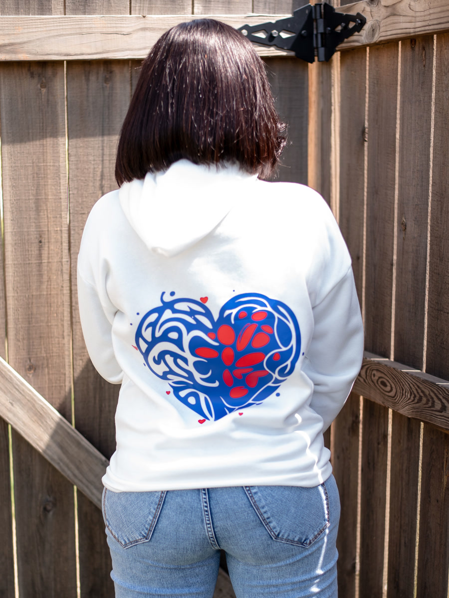 The back of the same white hoodie, printed with a large heart drawn in looping blue and red lines.