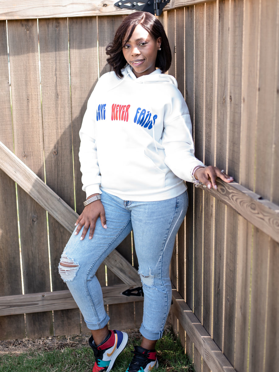 A white hoodie printed across the chest with love never fails in red and blue block letters.