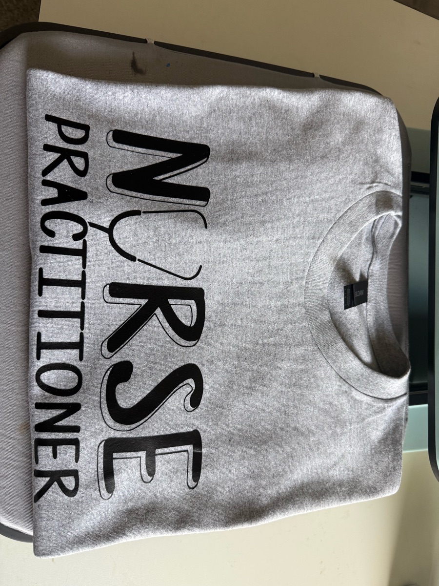 A heather grey sweatshirt lying on its side, printed NURSE in black outline letters with a stethoscope for the U and PRACTITIONER running beside it.