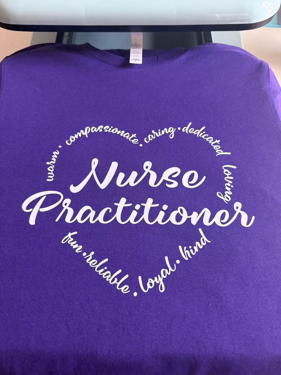 A purple tee on the heat press, printed Nurse Practitioner in white script inside a heart of words like caring, loyal and kind.