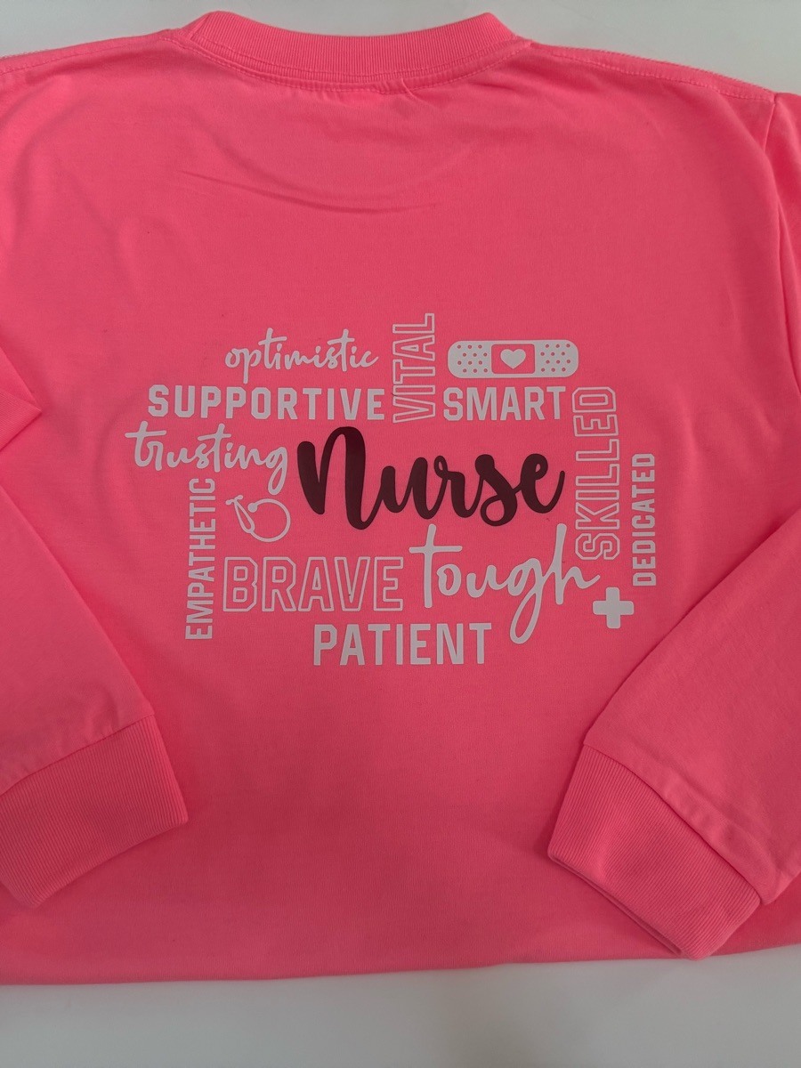 A coral long-sleeve tee printed Nurse in script inside a cloud of words like supportive, brave, tough and patient.
