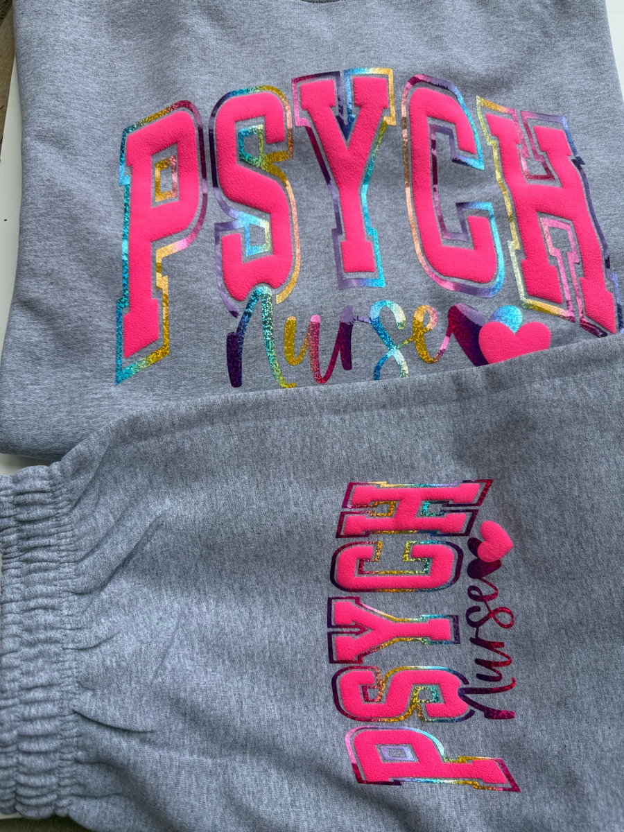 A heather grey sweat set printed PSYCH nurse in hot pink and rainbow foil letters, on the sweatshirt and again down the jogger leg.