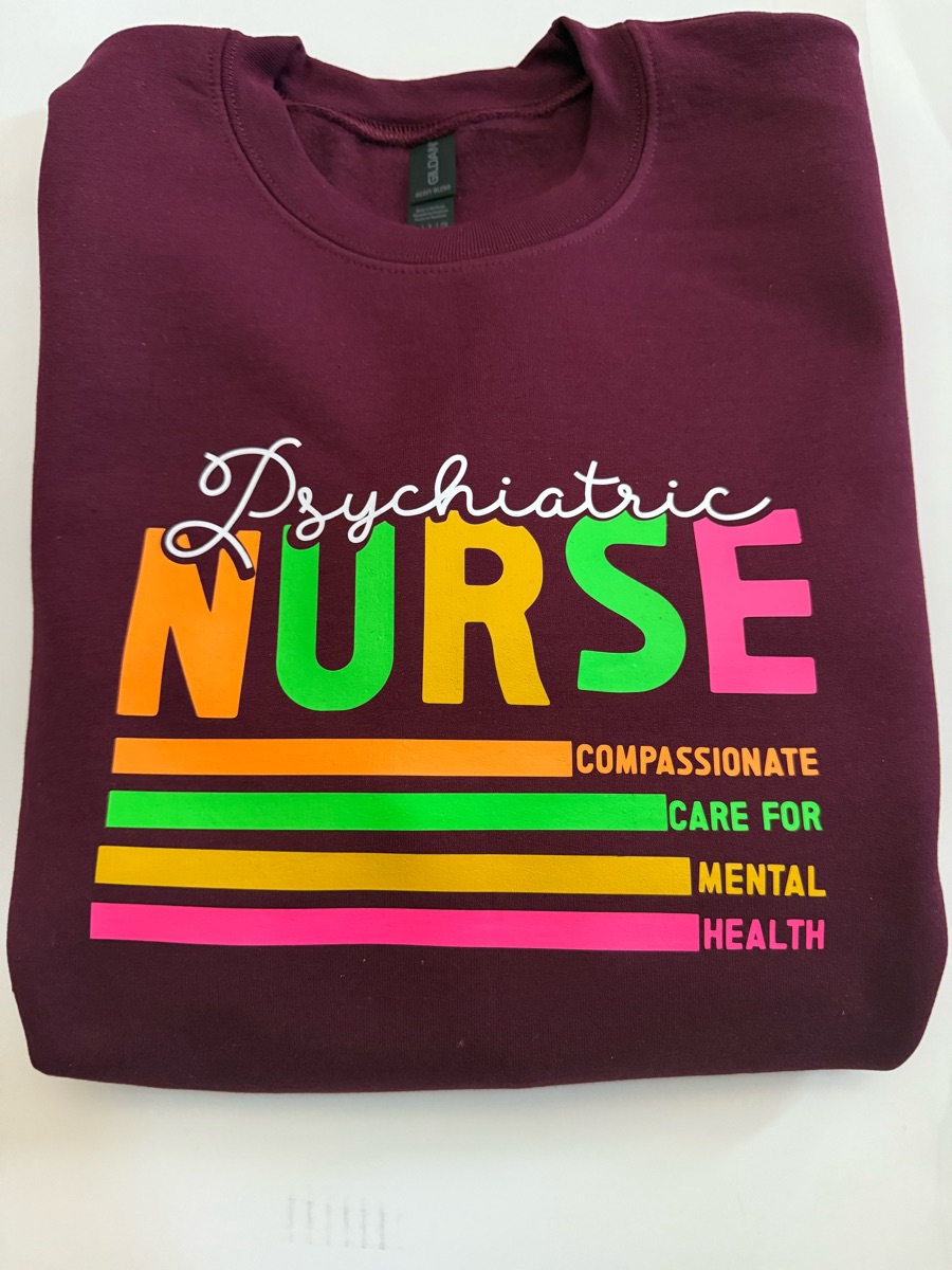 A maroon sweatshirt printed Psychiatric in white script over NURSE in orange, yellow, green and pink, with four bright stripes reading compassionate care for mental health.