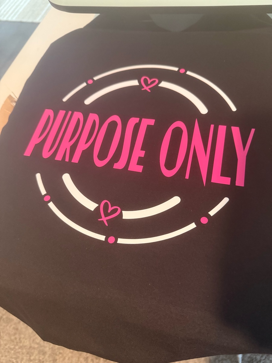A black tee printed PURPOSE ONLY in hot pink inside broken white circles with two small hearts.