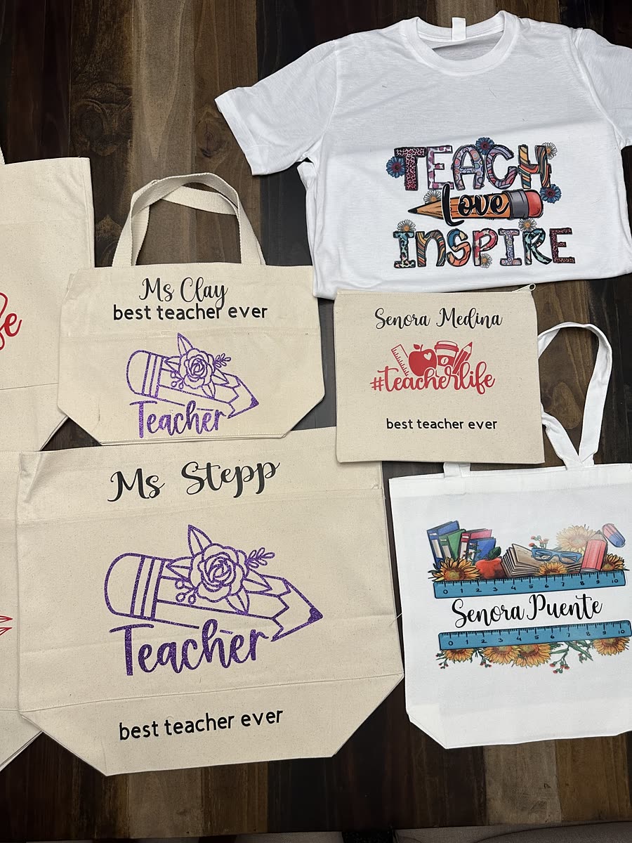 Four canvas totes, each printed with a different teacher's name above best teacher ever, beside a teach love inspire tee.