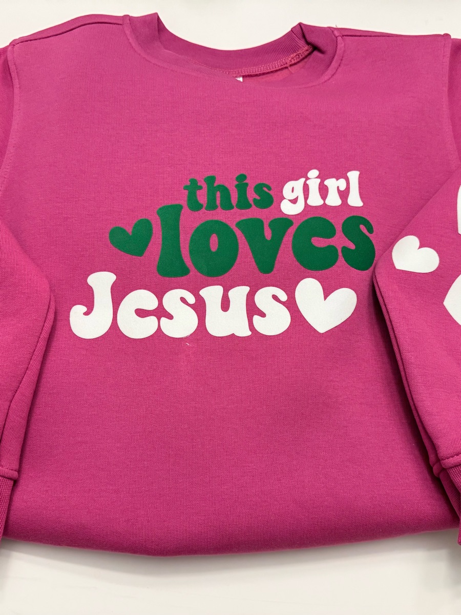 A magenta sweatshirt printed this girl loves Jesus in green and white, with white hearts on the sleeve.