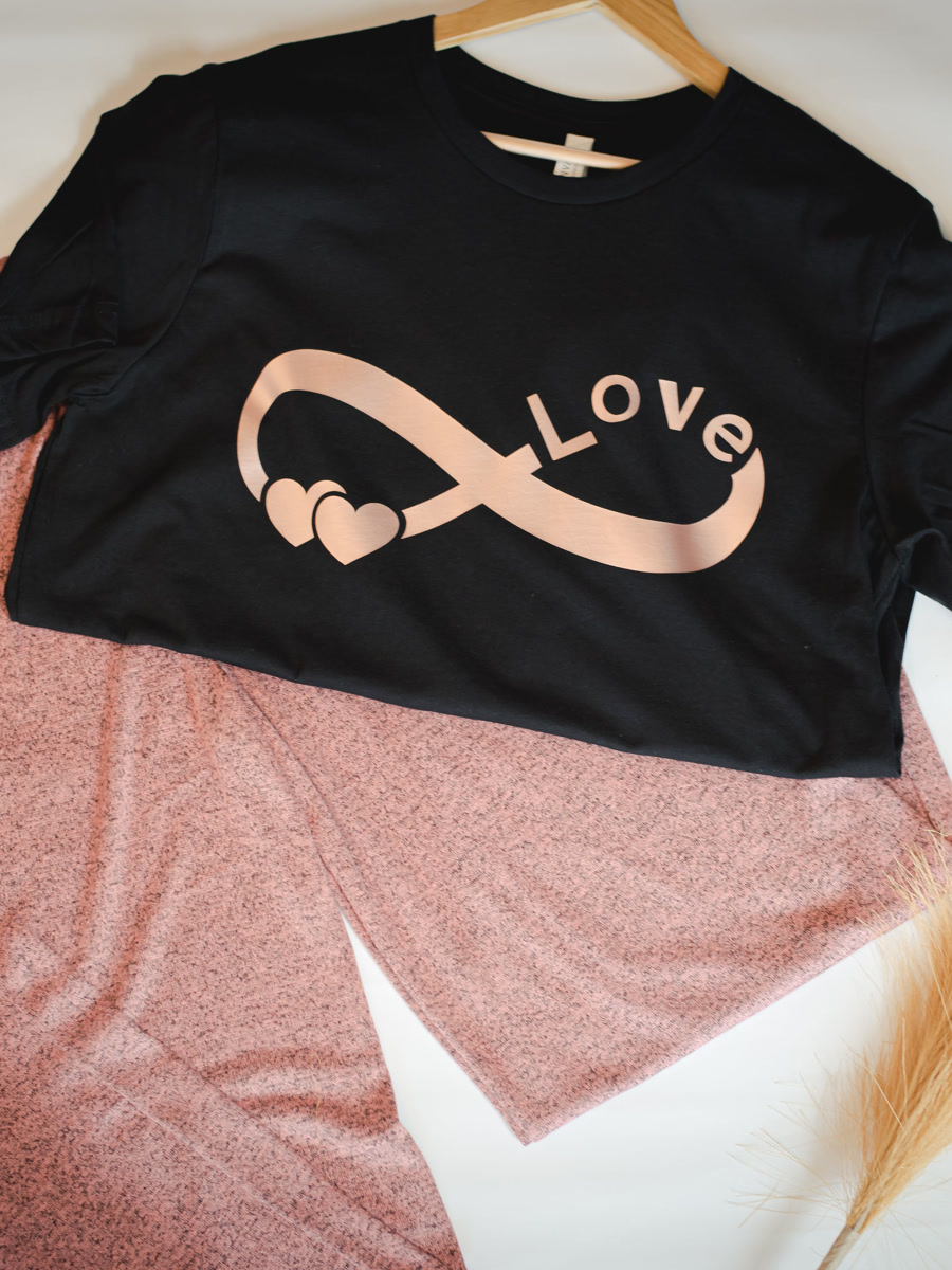 A black tee with a rose gold love infinity print, laid with a blush set.